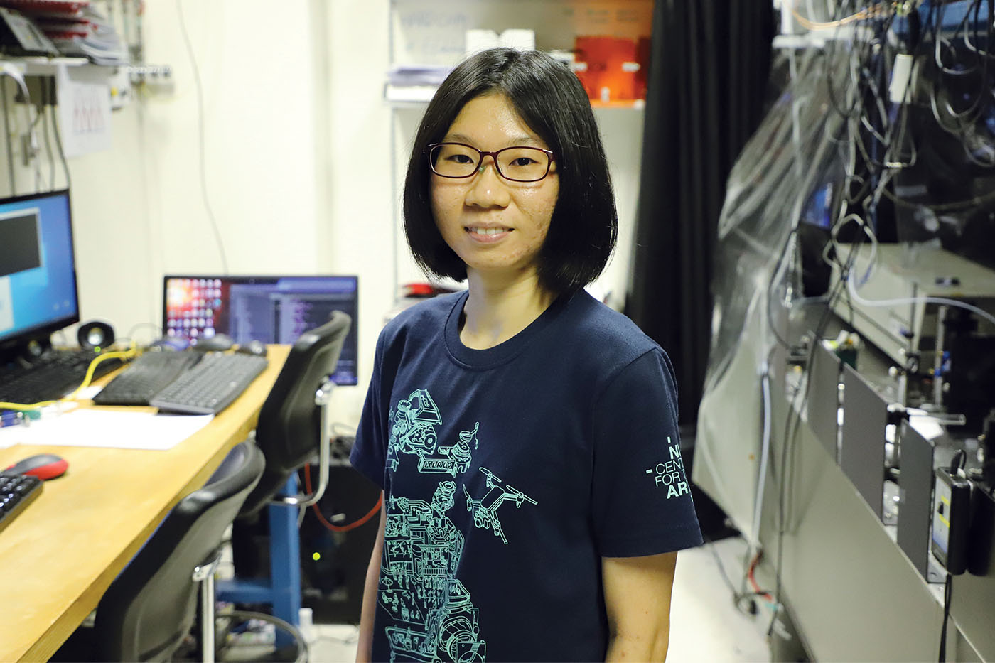 Researcher in laboratory at the Centre for Quantum Technologies Singapore, standing between computer control desk and black optical benches