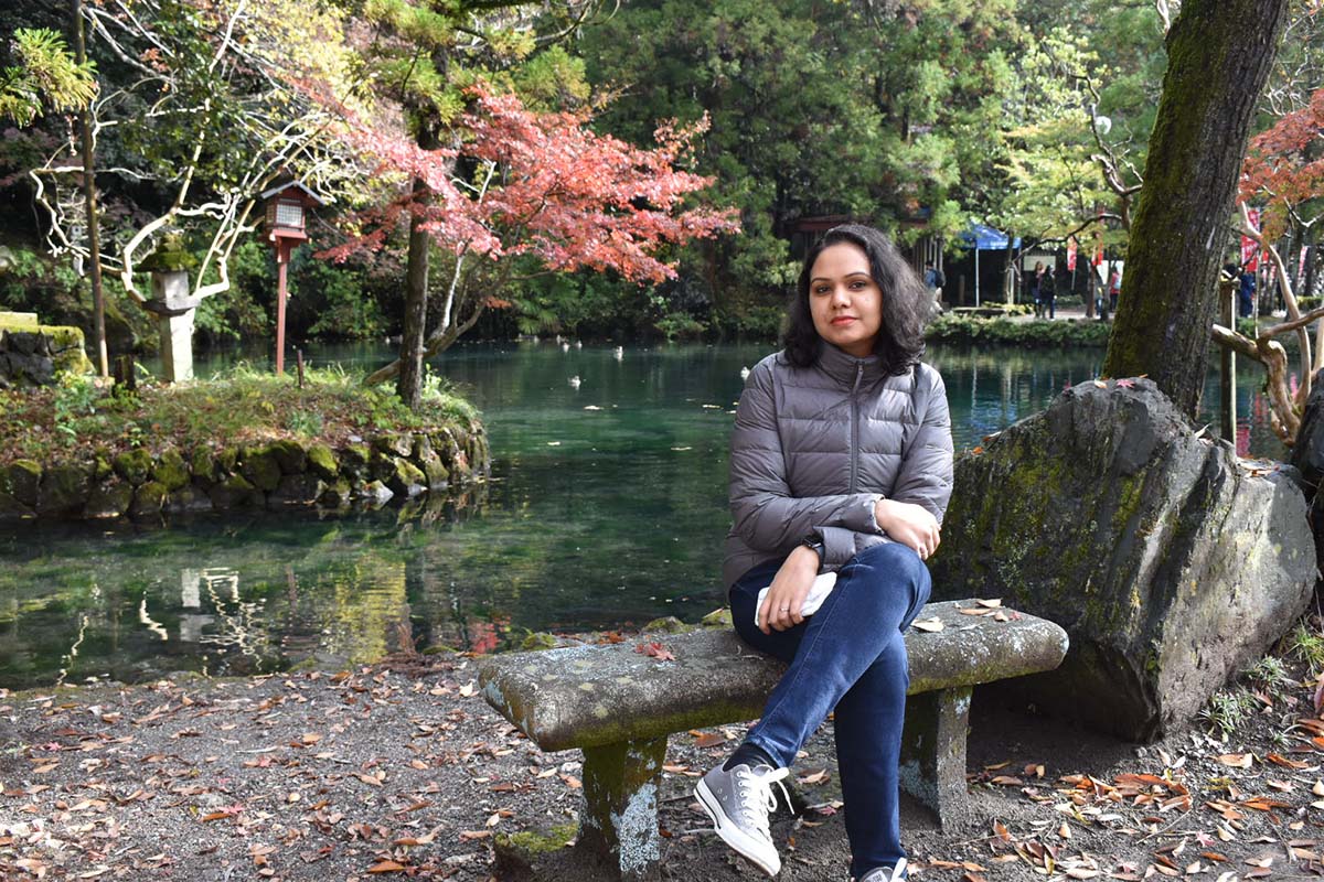 Resmi sits on a stone bench in front of a lake