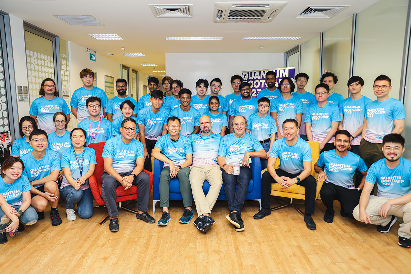 Posed group photo of people involved in planning Quantum Bootcamp 2023. The picture is posed indoors and everyone is wearing the bootcamp t-shirt in pale blue and pink.